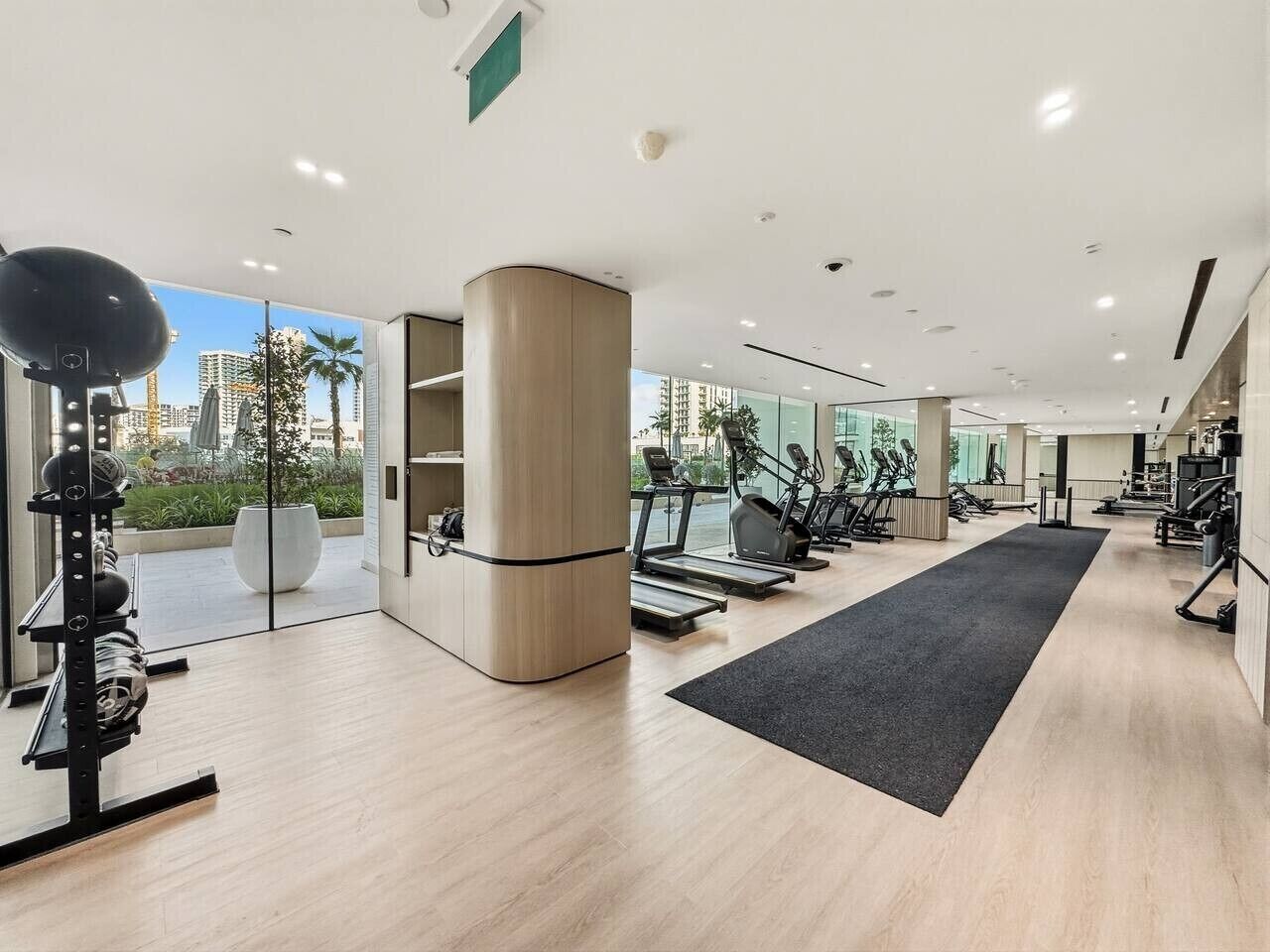 Une salle de sport moderne équipée de machines de cardio, dotée d’un grand miroir et offrant une vue sur la ville.