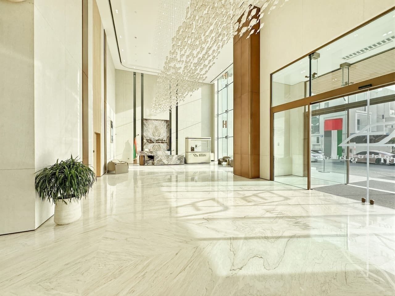 A spacious lobby with a marble floor, a potted plant, and a large glass window offering a view of the street.
