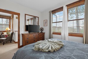 A bedroom with a bed, a dresser, a TV, and a window with blinds.