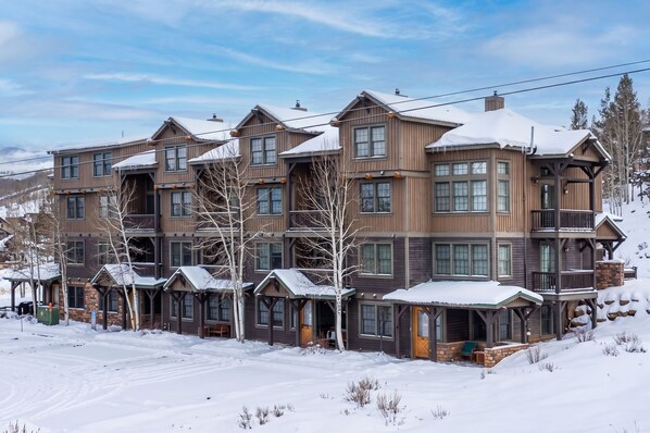 A multi-story wooden building with a snow-covered roof, large windows, and a covered outdoor seating area.