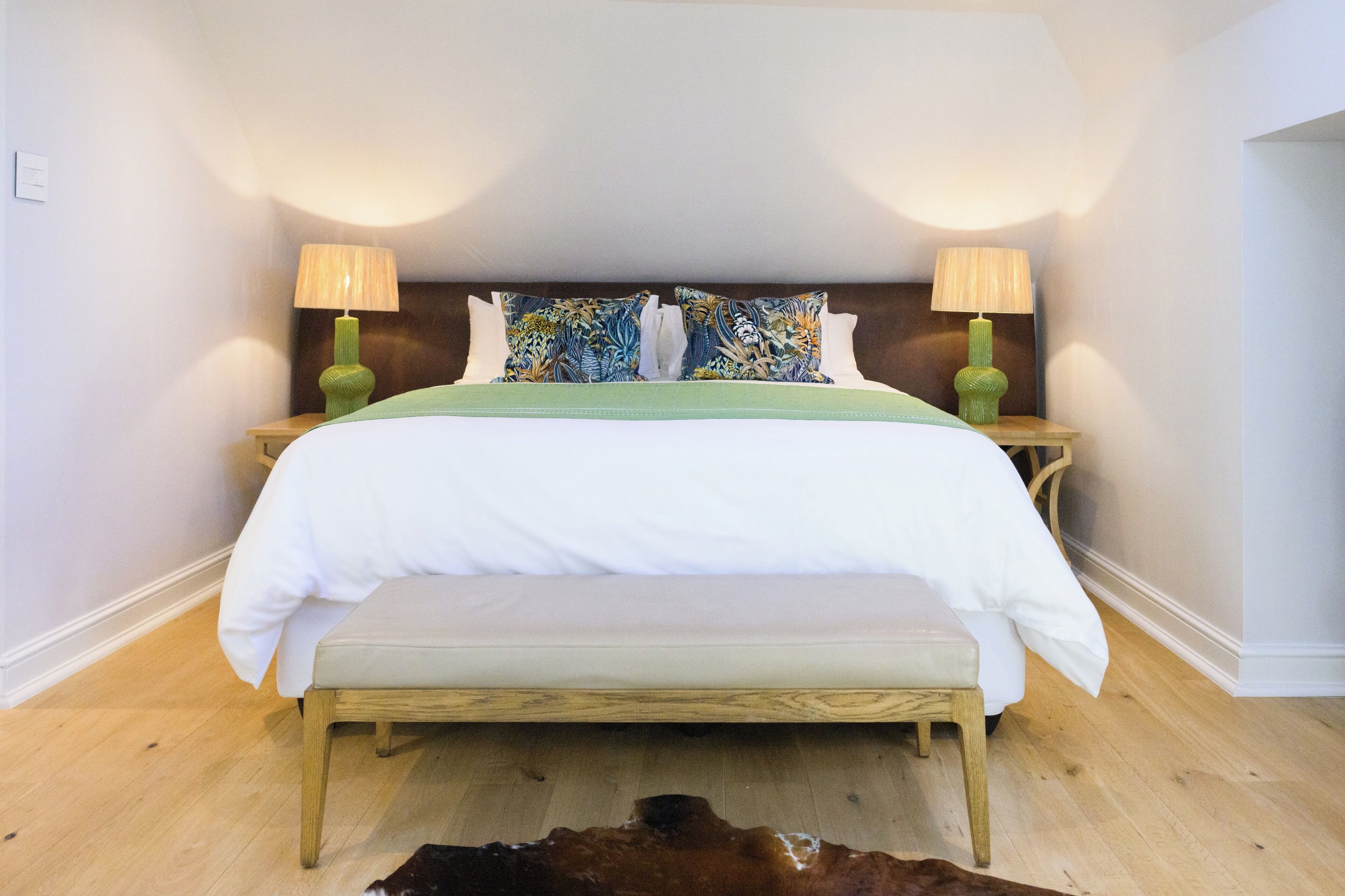 A neatly made bed with a green bedspread and white pillows, flanked by two wooden nightstands with lamps.