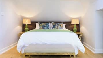 Cama bem arrumada com colcha verde e almofadas brancas, acompanhada por duas mesinhas de cabeceira de madeira com luminárias.