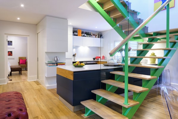 Eine moderne Küche mit einer zentralen Kochinsel, einer Treppe mit grünen Akzenten und einem Essbereich mit einer rot gepolsterten Bank.