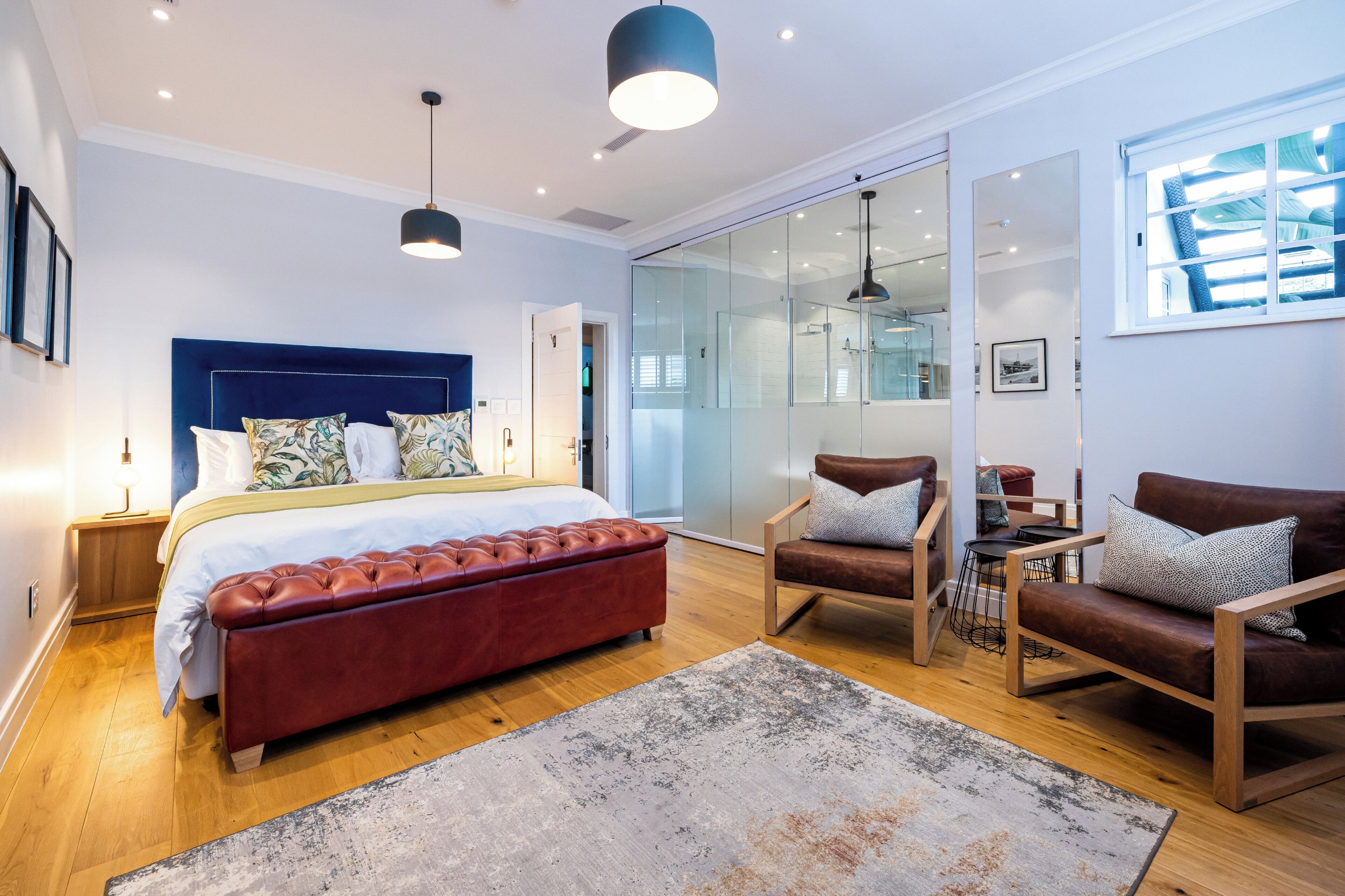 A modern bedroom with a large bed, a glass shower, a seating area with chairs, and a view of the outdoors.