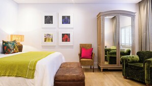 Una habitación de hotel con cama, una silla, armario y obras de arte en la pared.