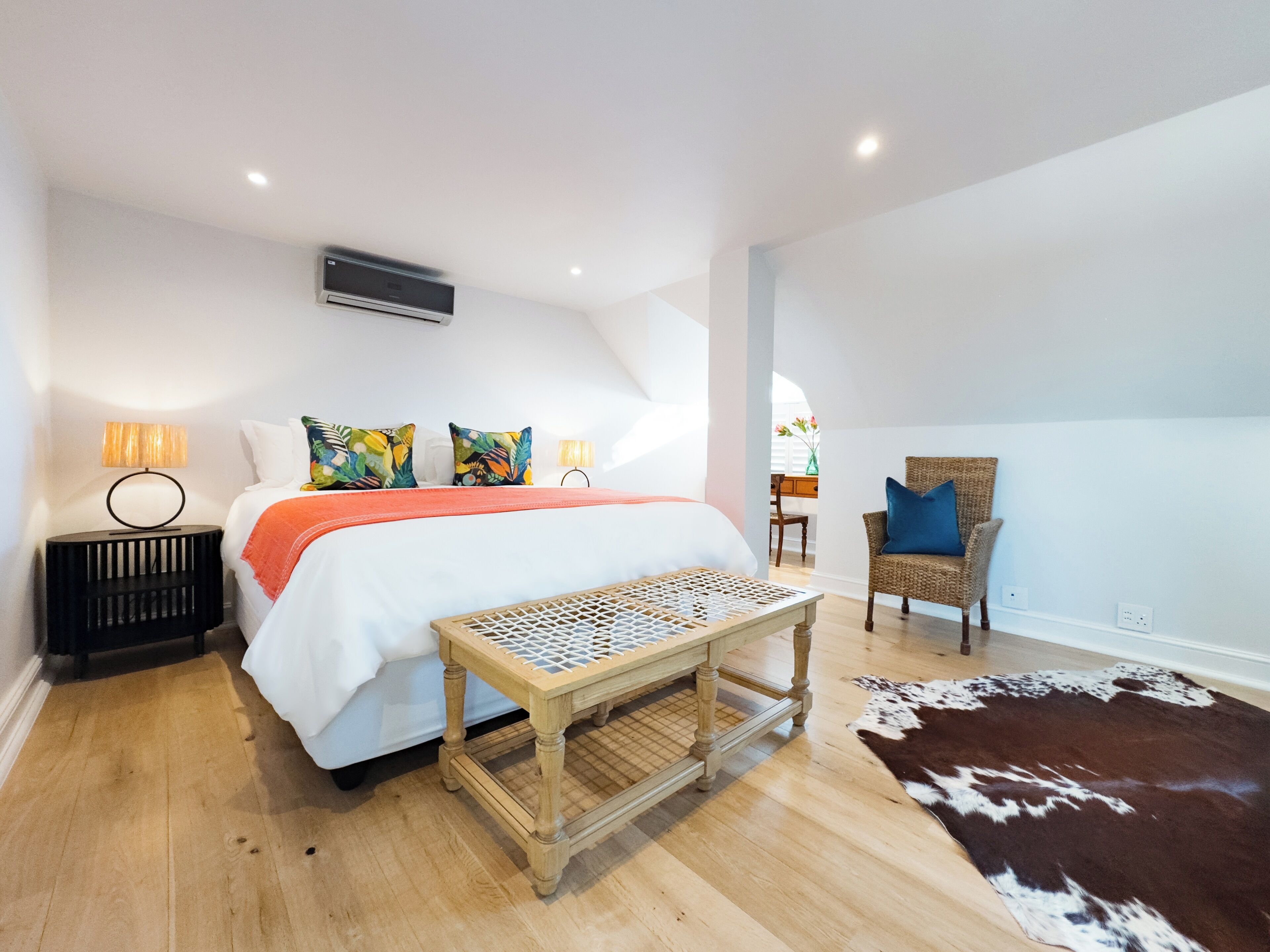 A bedroom with a bed, a small table, a chair, a rug, and a window.