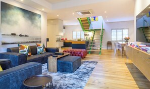 A modern living room with a sofa, ottoman, and coffee table, a painting on the wall, and a staircase with a green railing. - Rozenhof Villas (Stellenbosch)