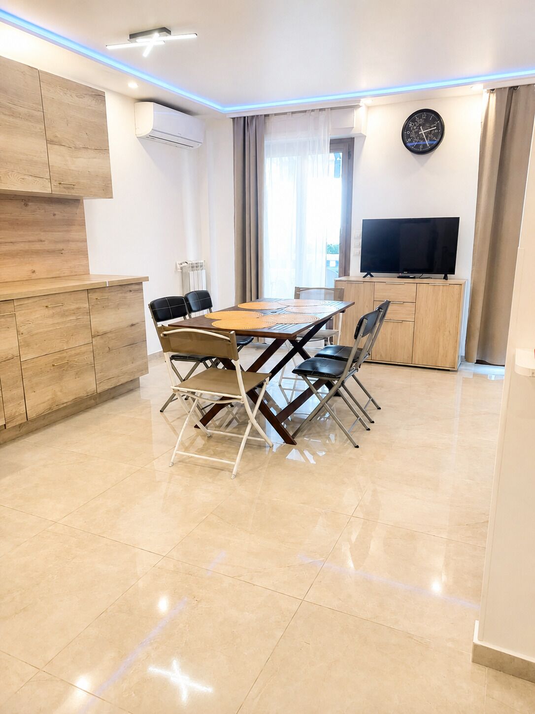 Un salon moderne avec une table à manger, des chaises, un téléviseur à écran plat et une horloge au mur.