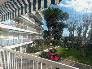 Un immeuble à plusieurs étages doté de balcons, une voiture rouge garée dans l’allée, et une pelouse bien entretenue avec des arbres.