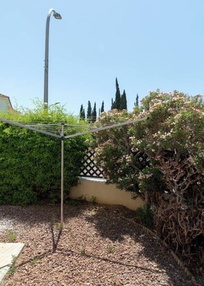 Ein Garten mit einer Metallkonstruktion, möglicherweise zum Wäschetrocknen, umgeben von dichtem Buschwerk und einem Zaun.