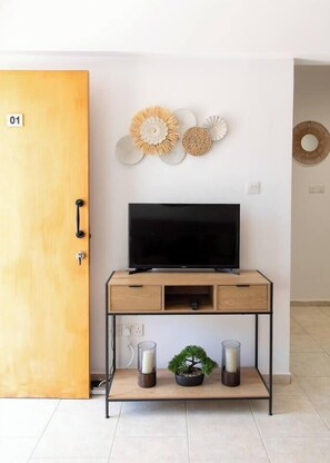 Ein Zimmer mit Holztür mit der Aufschrift '01', einem Fernseher auf einem Holzboden, einer kleinen Pflanze und Wanddekoration.