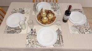 Uma mesa de jantar posta com pratos, talheres, copos, uma garrafa de vinho e uma tigela de comida.