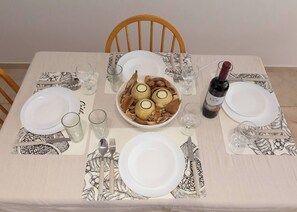 Ein Esstisch mit Geschirr, Besteck, Gläsern, einer Weinflasche und einer Schüssel mit Essen.
