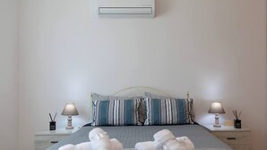 Cama bem arrumada com almofadas e toalhas, luminária de cabeceira e ar-condicionado fixado na parede.