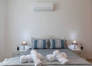 Ein ordentlich bezogenes Bett mit Kissen und Handtüchern, eine Nachttischlampe sowie eine Wand-Klimaanlage.