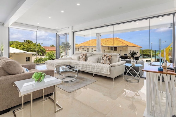 Settle into your bright, modern living space where floor-to-ceiling windows frame coastal views and gentle breezes flow through. Your open, sunlit sanctuary invites relaxation with sleek furnishings and serene elegance.