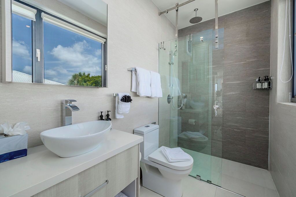 Un baño moderno con un lavamanos de diseño, un inodoro y una zona de ducha con mampara de vidrio.