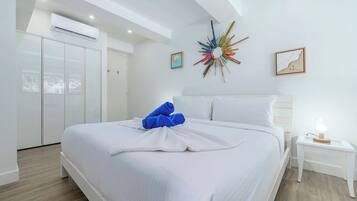 A hotel room with a bed, white walls, a ceiling fan, and a decorative wall piece.