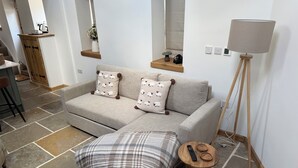 Ein modernes Wohnzimmer mit einer Couch, einer karierten Decke, einem kleinen Holznachttisch und einer Stehlampe.
