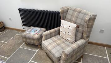 A room with a plaid armchair and ottoman, a radiator, and a newspaper on the ottoman.