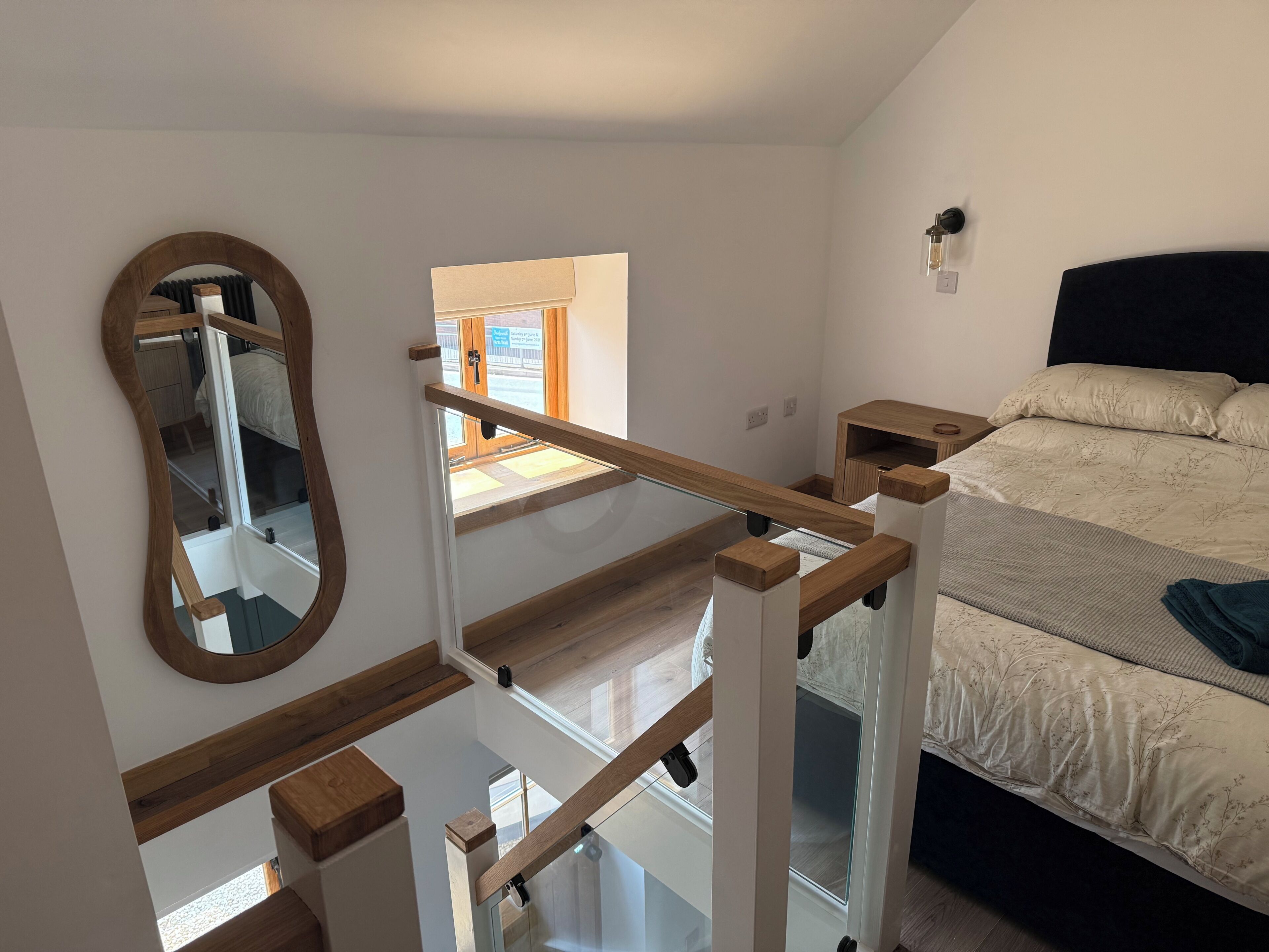 A bedroom with a bed, a nightstand, a mirror, and a window.
