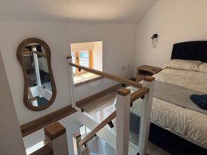 Un dormitorio con cama, mesita de noche, espejo y ventana.