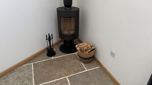 Ein Eckzimmer mit einem schwarzen Kaminofen, einem Kerzenhalter und einem Holzkorb.