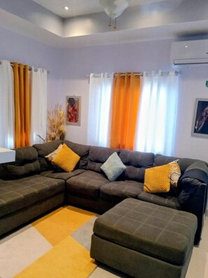A living room with a sectional sofa, a small ottoman, and a yellow rug. - Your Jamaican Getaway | Summer Breeze Villa with Pool & Gym Access (Lucea)