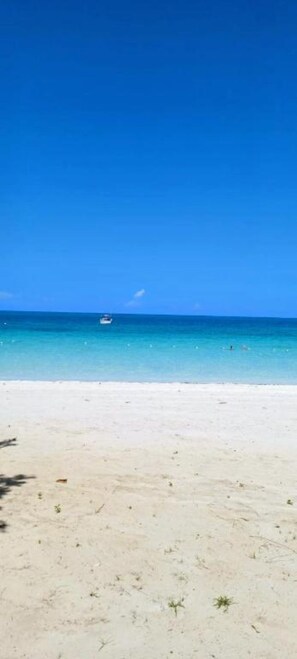 A beach with clear blue water and a boat in the distance. - Your Jamaican Getaway | Summer Breeze Villa with Pool & Gym Access (Lucea)