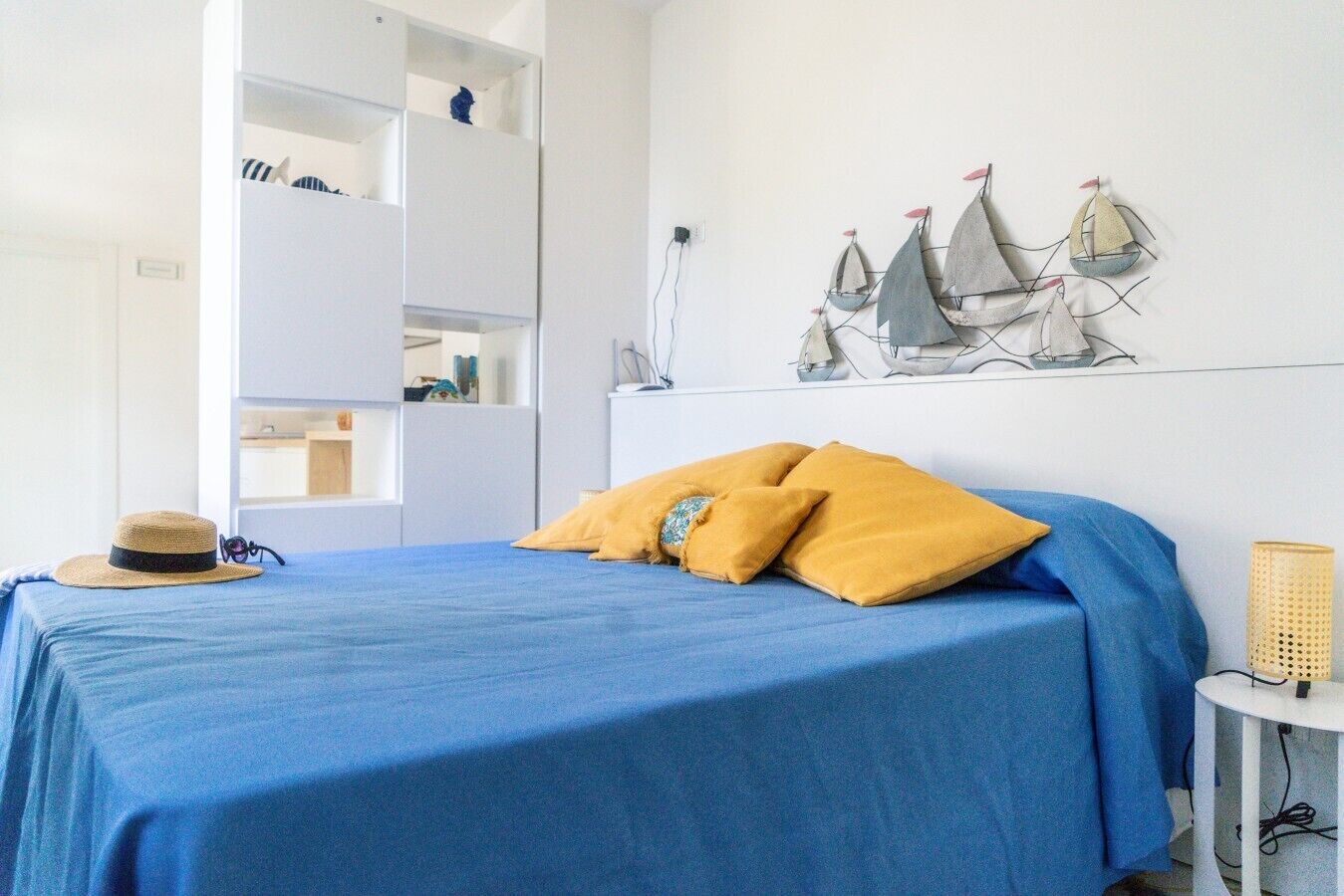 Un lit recouvert d’une couverture bleue et orné de deux oreillers jaunes, un chapeau de paille et un mur décoré de motifs représentant des voiliers.