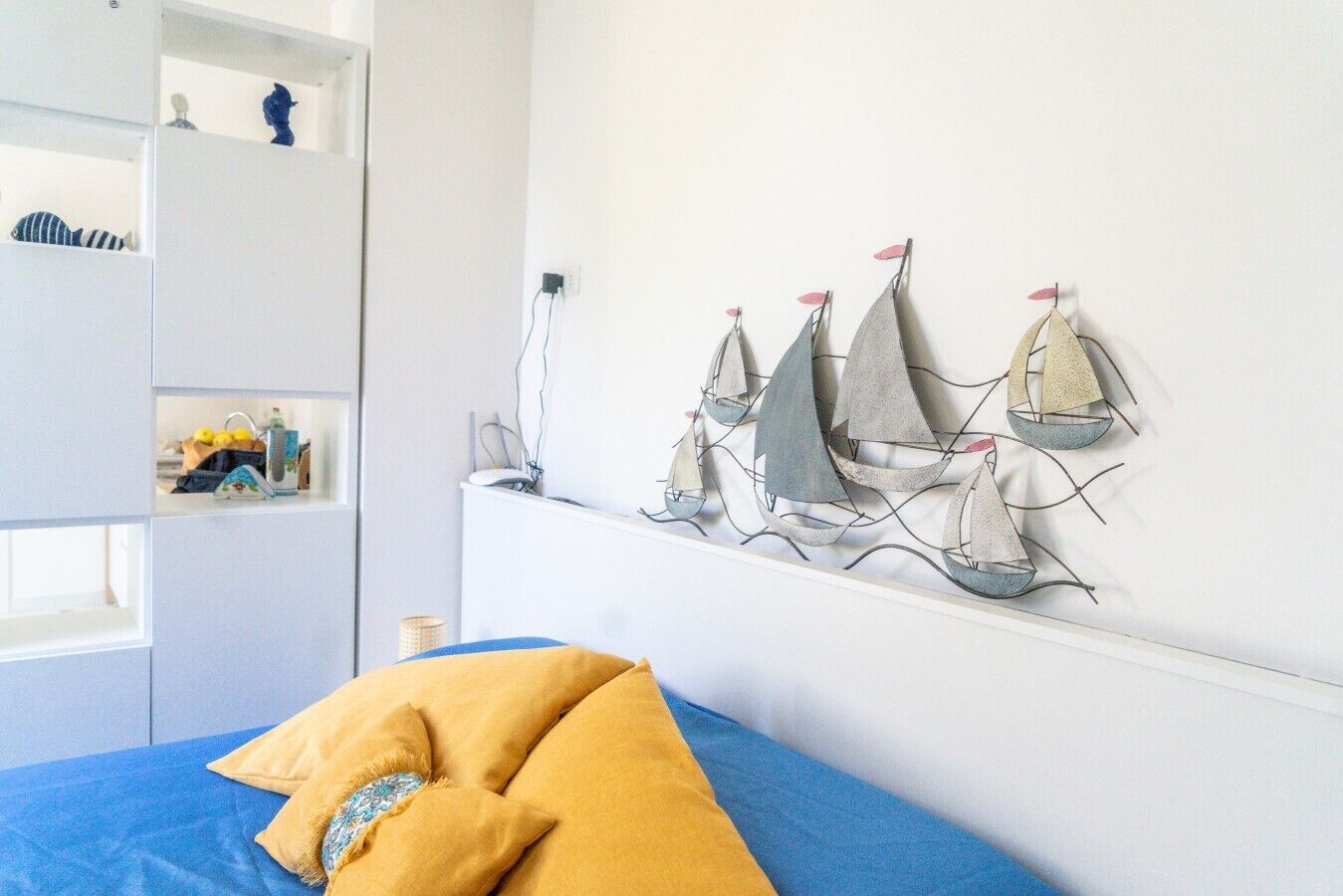 Een slaapkamer met een bed, een aan de muur bevestigde decoratie van een zeilboot, en een plank met spullen.