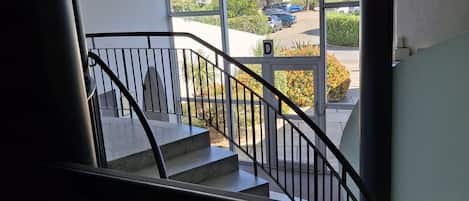 Eine Treppe mit Metallgeländer führt zu einem Außenbereich mit Blick auf geparkte Autos und Grünflächen.