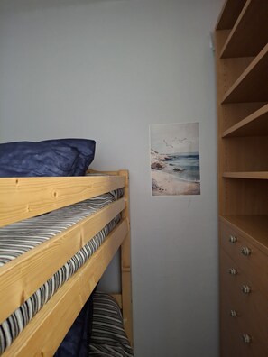 Un lit superposé avec une literie à rayures, une étagère fixée au mur et un tableau représentant une scène de plage.