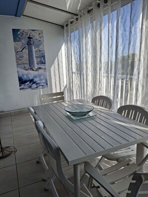 A dining area with a table and chairs, a glass bowl centerpiece, and a painting of a lighthouse on the wall. - Studio apartment with a loggia near the ocean (Le Grau-du-Roi)