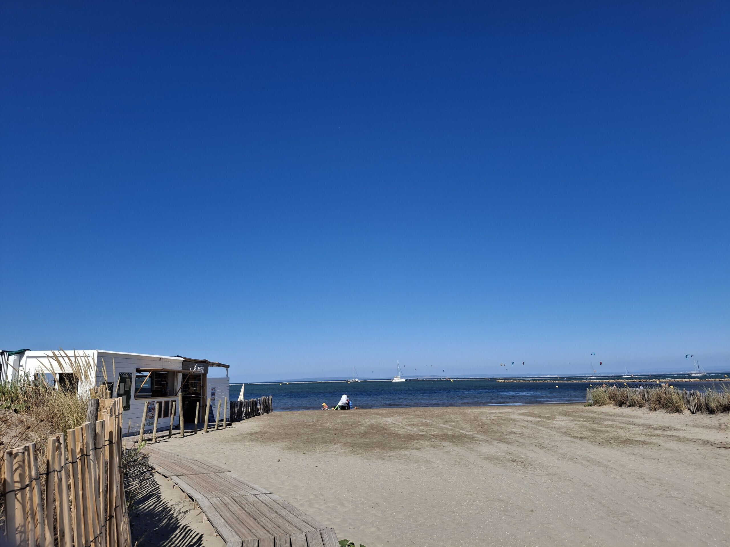 A beach with a wooden boardwalk, a small white building, and a clear blue sky.