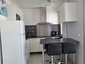 A compact kitchen with a refrigerator, a stove, a sink, and a dining area with two chairs. - Studio apartment with a loggia near the ocean (Le Grau-du-Roi)