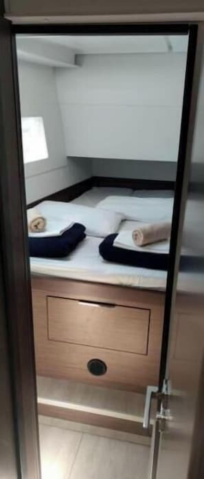A compact room with a bed, a small wooden drawer, and a window.