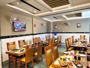 Um restaurante com várias mesas, cadeiras e uma televisão exibindo notícias.
