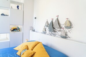 Une chambre à coucher avec un lit, une décoration murale représentant un voilier et une étagère contenant divers objets.