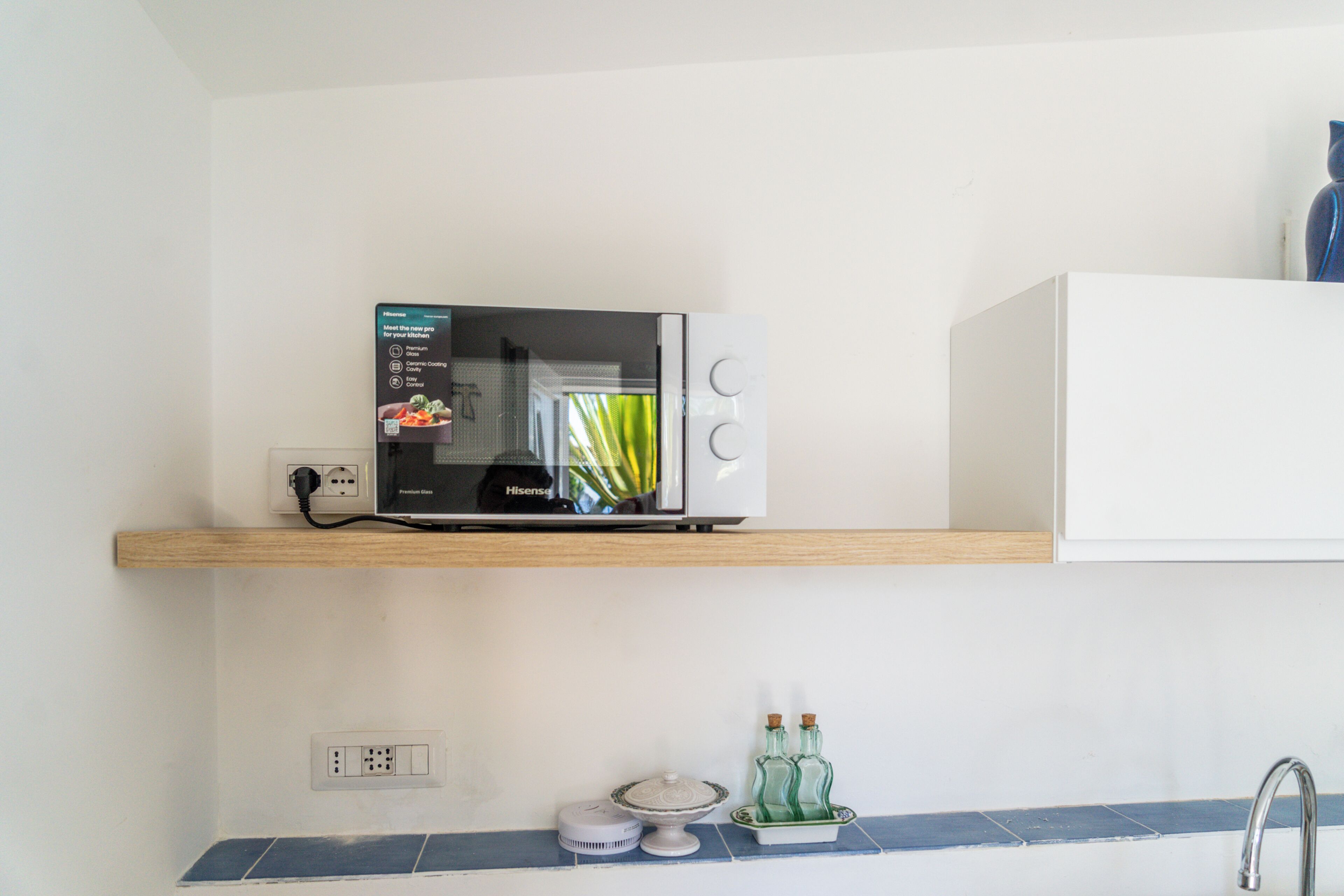 Una cocina con microondas en un estante de madera, un lavamanos con grifo y una encimera con dispensador de jabón para lavar platos.