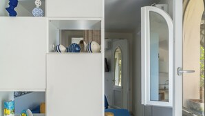A room with a white door, a blue bedspread, and a shelf with decorative items. - Naos Nerano (Nerano)