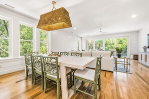 A spacious room with a dining area featuring a white table and green chairs, large windows with a view of trees, and a ceiling fan. - Private Pool, Elevator, Close to Beach, New Construction, King Beds, SS0298 (Southern Shores)