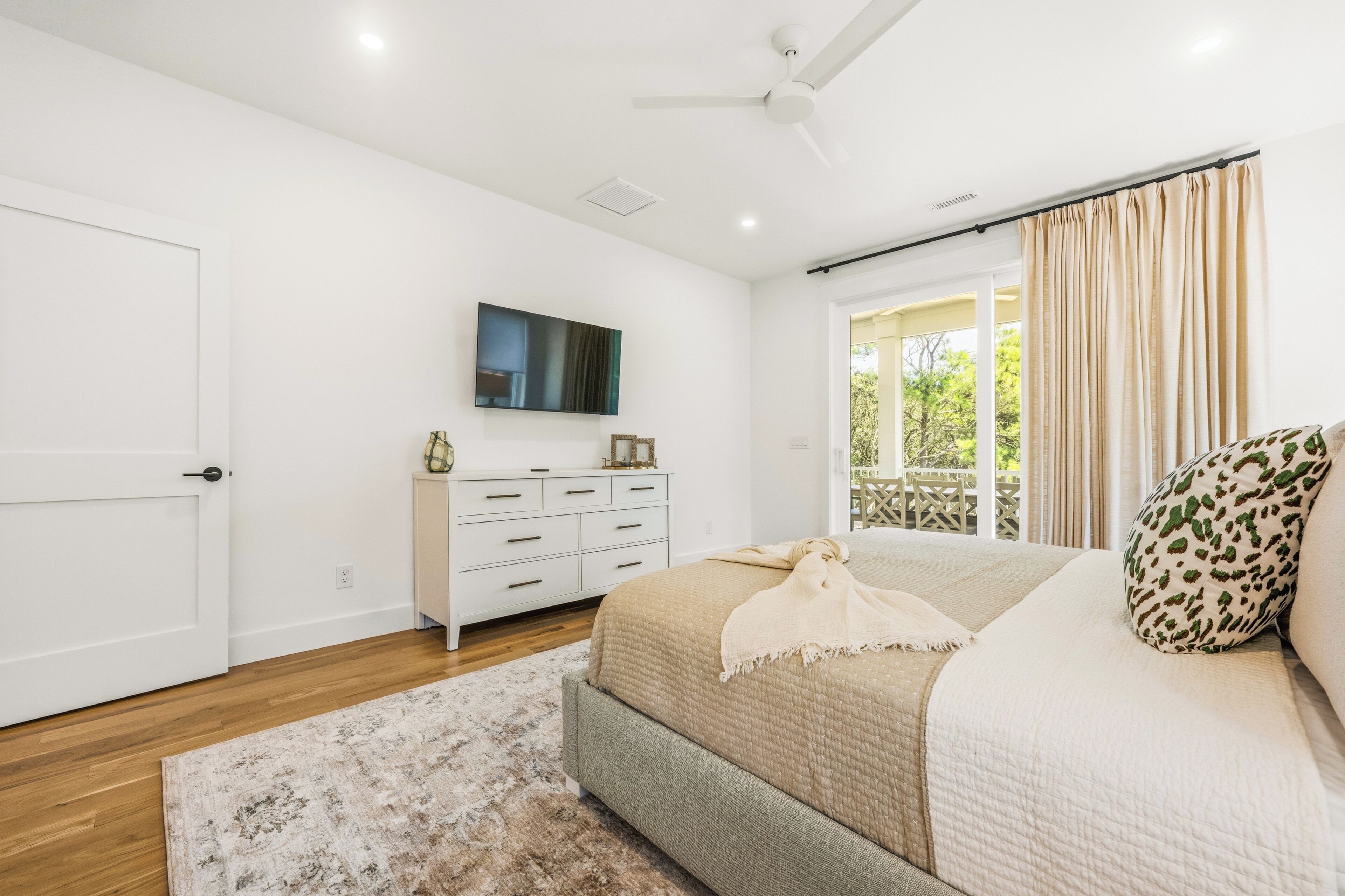 Une chambre à coucher avec un lit, une commode, un téléviseur et une fenêtre avec des rideaux.