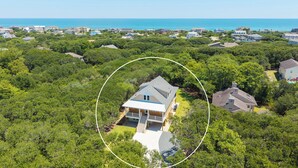 Et boligområde med et hus omgivet af frodig vegetation og udsigt til havet.
