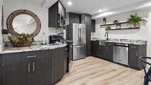 Eine moderne Küche mit dunklen Schränken, Edelstahlgeräten, einer Marmorarbeitsplatte und einem spiegelnden Wandbild mit Holzrahmen.