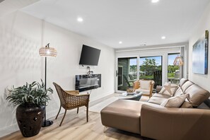 A modern living room with a flat-screen TV, wicker furniture, a leather sofa, and a view of the outdoors through a glass door. - 122 Edgewater Inn offers 3 bedrooms and beautiful waterfront views (Charlevoix)