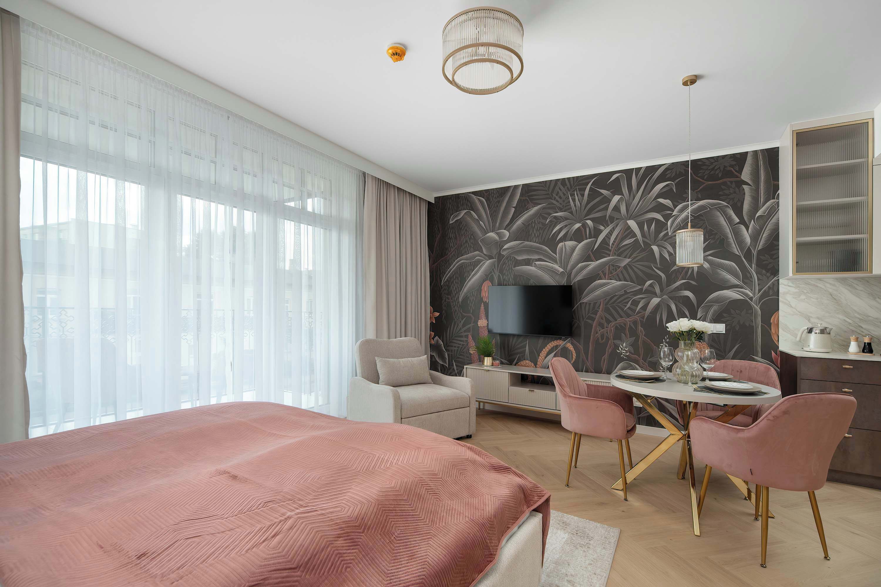 A modern bedroom with a large bed, a dining table with chairs, a TV, and a decorative wall.