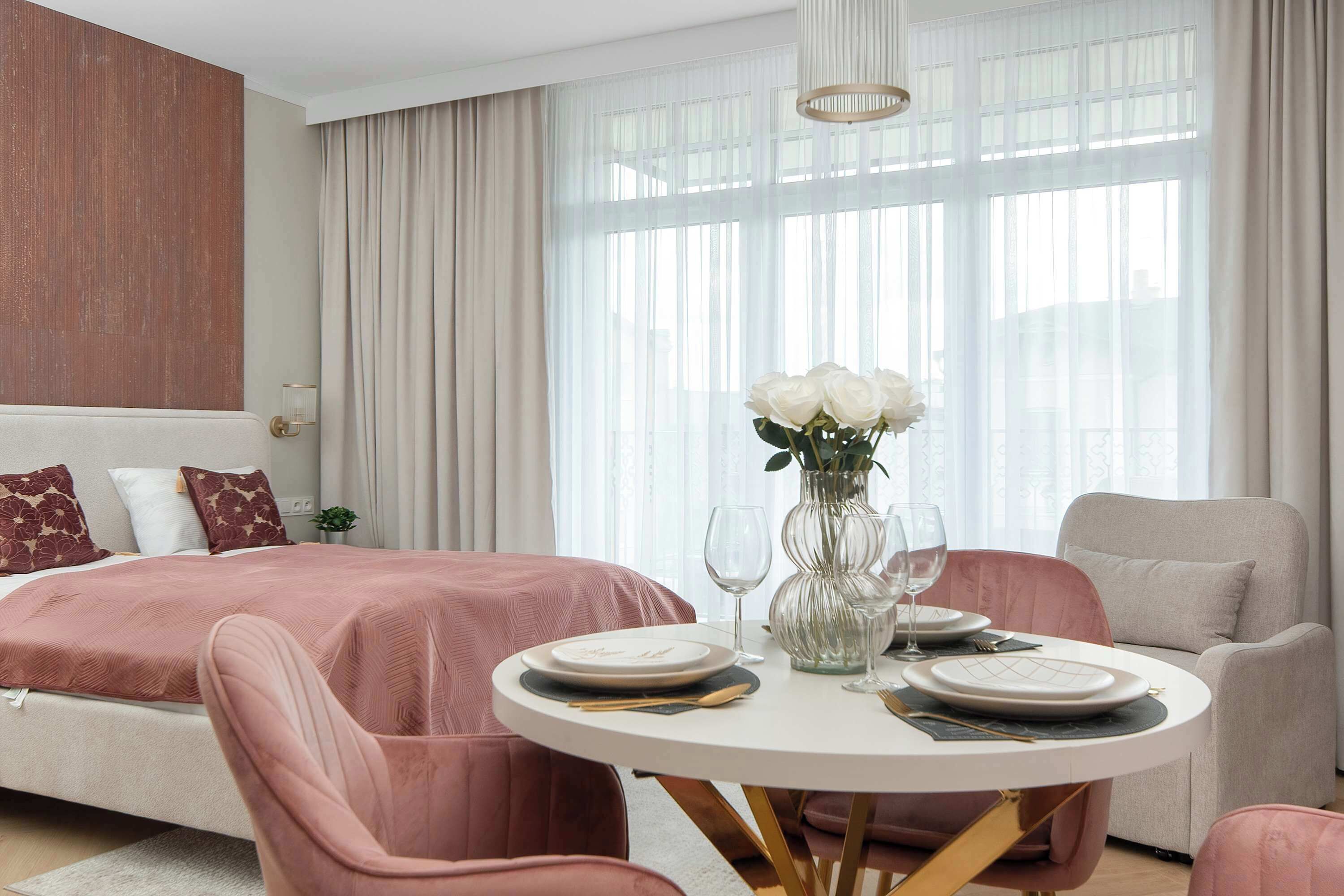 Quarto moderno com cama, mesa de jantar redonda com pratos e copos, e um vaso com flores.