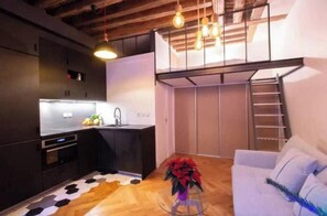 A compact living space with a kitchenette, a dining area with a patterned rug, a white sofa, and a staircase leading to an upper level. - Beautiful, Air-Conditioned Apartment in Aix, Right in the Heart of Downtown (ile de france)