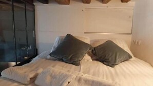 Een bed met een witte spreiding en twee kussens, een houten plafond en een witte muur.